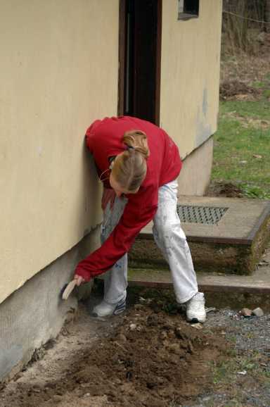 Anja Hesse, Klasse MDQM II, 2. Ausbildungsjahr, reinigt den freigelegten Sockel eines der Bungalows in Schneckenmühle mit der Drahtbürste. April 2005. Klicken Sie auf das Bild, wenn Sie einen Schülerbericht über das Projekt lesen möchten!